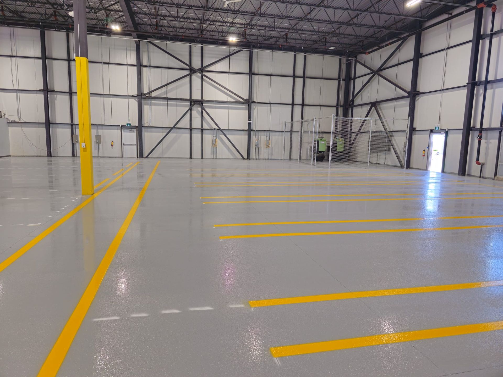 Large, empty industrial building with grey floors, yellow lines, and metal structure.