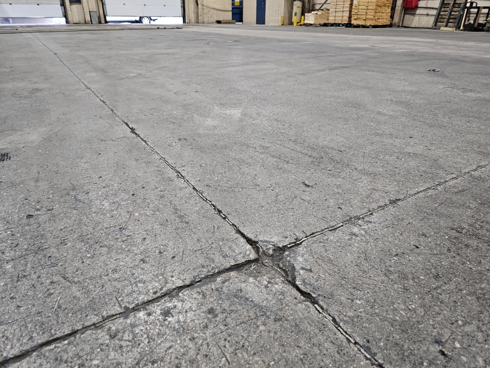 Cracked concrete floor with expansion joints in a warehouse setting, gray in color.