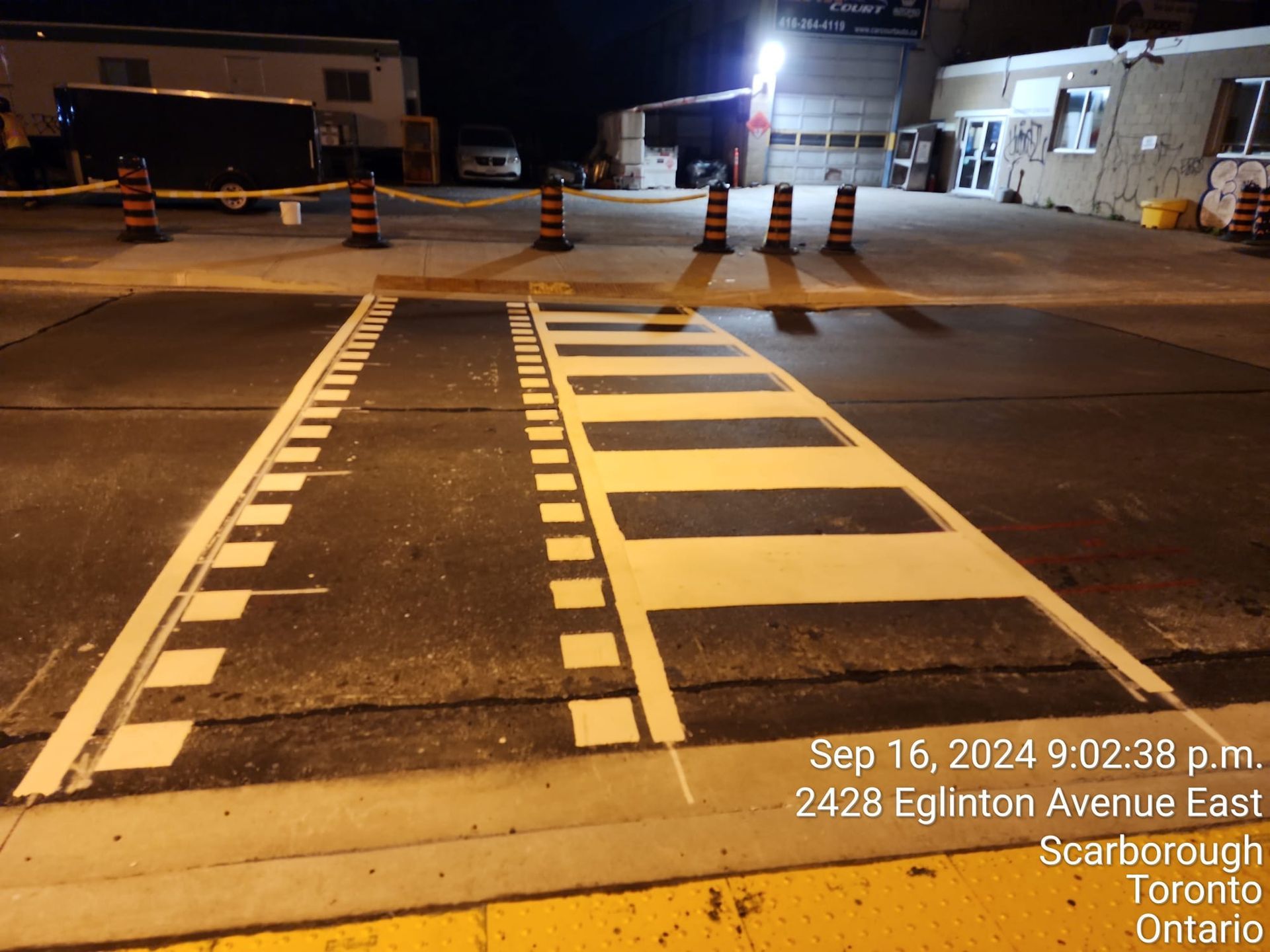 Newly painted crosswalk on Eglinton Avenue East at night, with traffic cones and building in background.