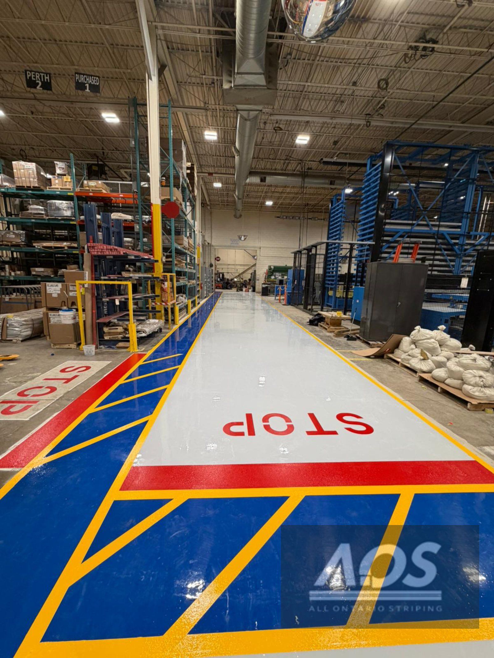 Warehouse floor with a long white pathway marked with blue and yellow lines.  