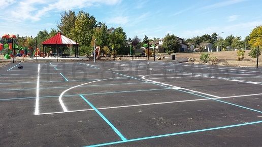 Playground with asphalt surface marked for games. Includes a red and white gazebo, trees, and colorful play structures.