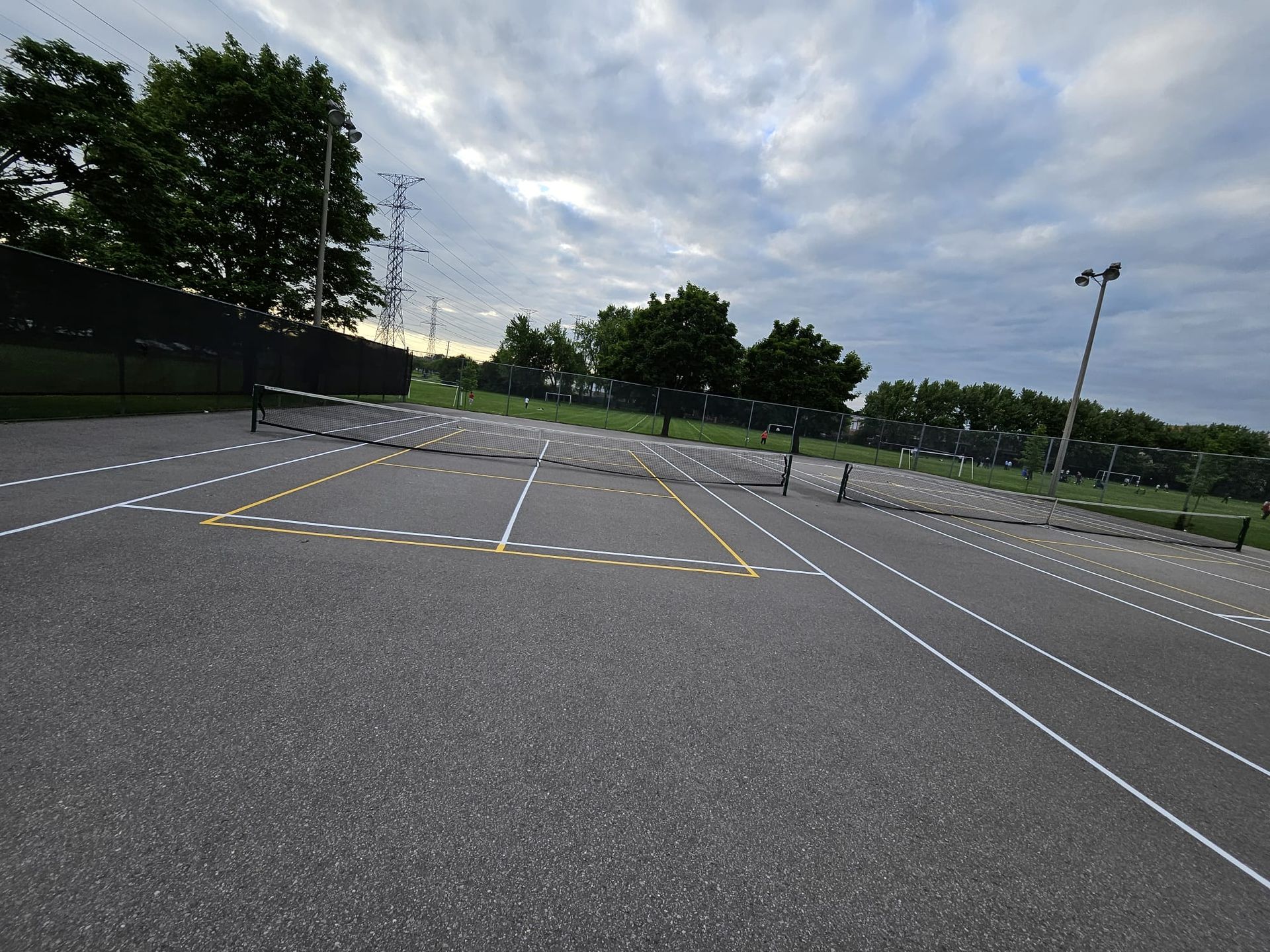 Outdoor tennis court with white and yellow lines, overcast sky.