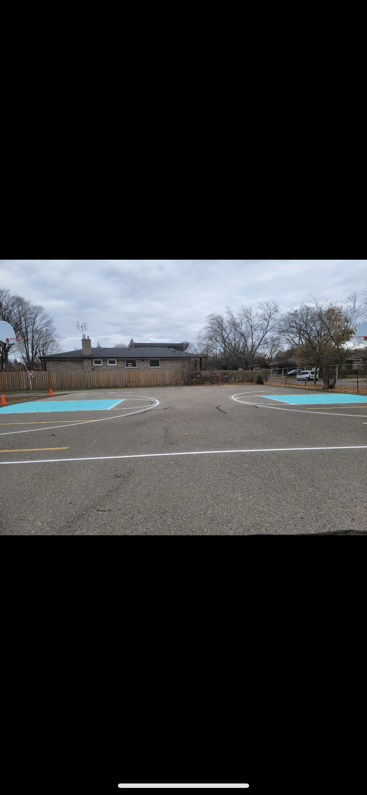 A paved area with white and blue markings, trees, and a building under a cloudy sky.