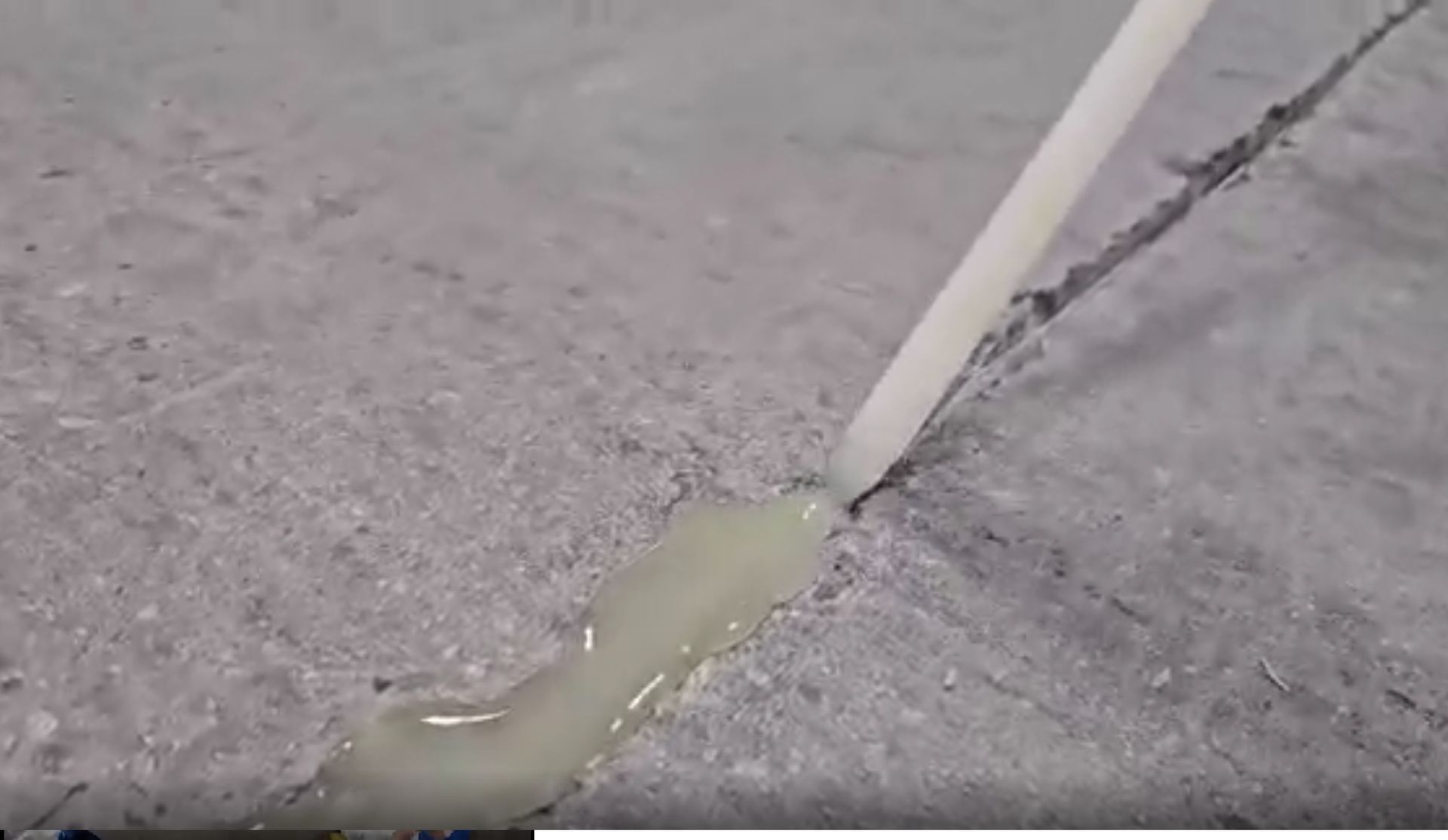 A white sealant is being applied to a crack on a concrete surface.