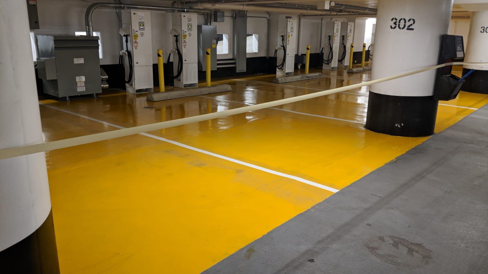 Yellow painted parking spots in an indoor parking garage with charging stations, and a white and black column.