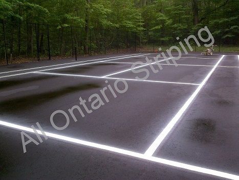 Asphalt surface with white lines marking tennis court. Trees in the background.
