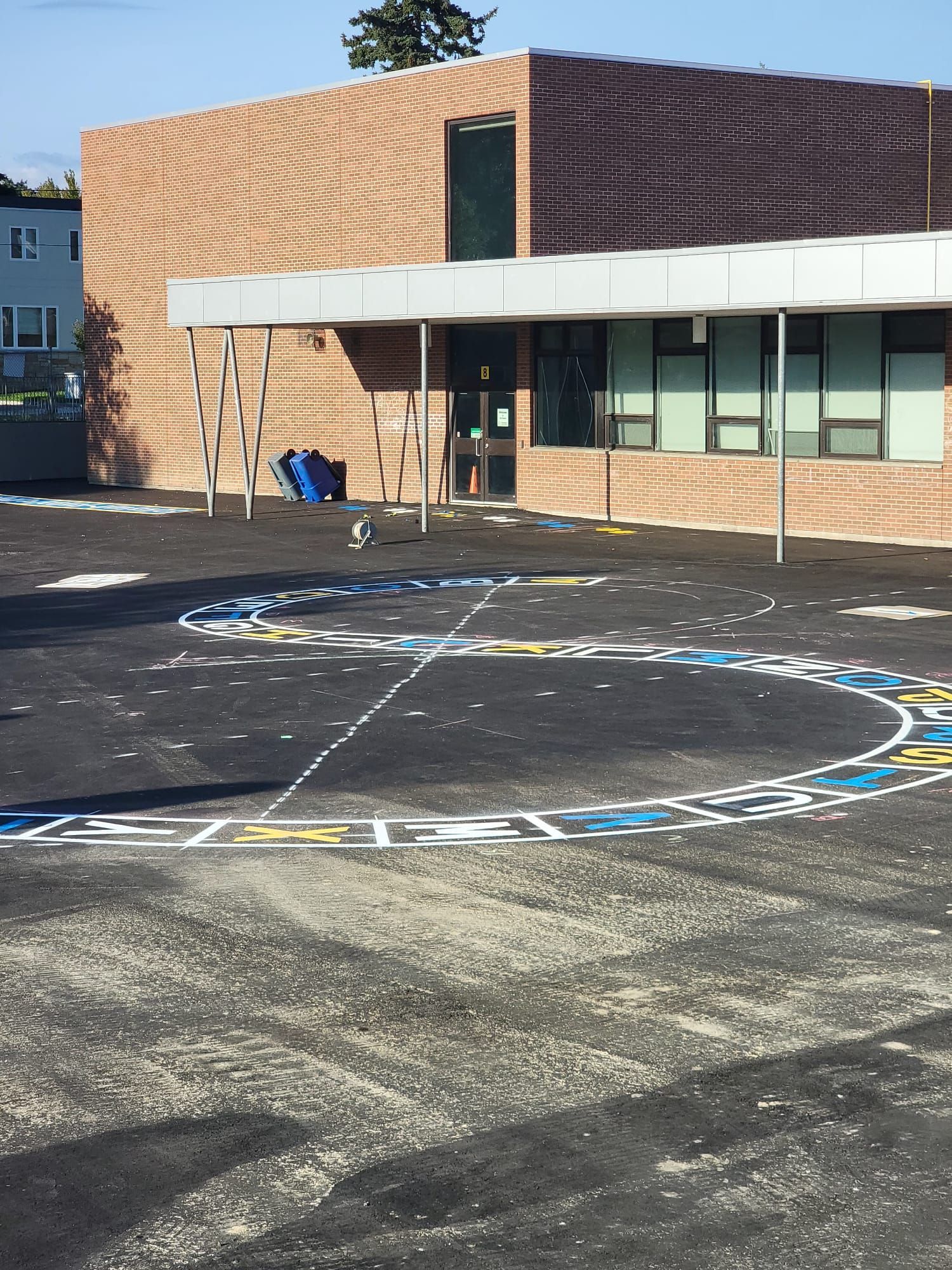 Schoolyard with a painted hopscotch game and a brick building with a covered entrance.