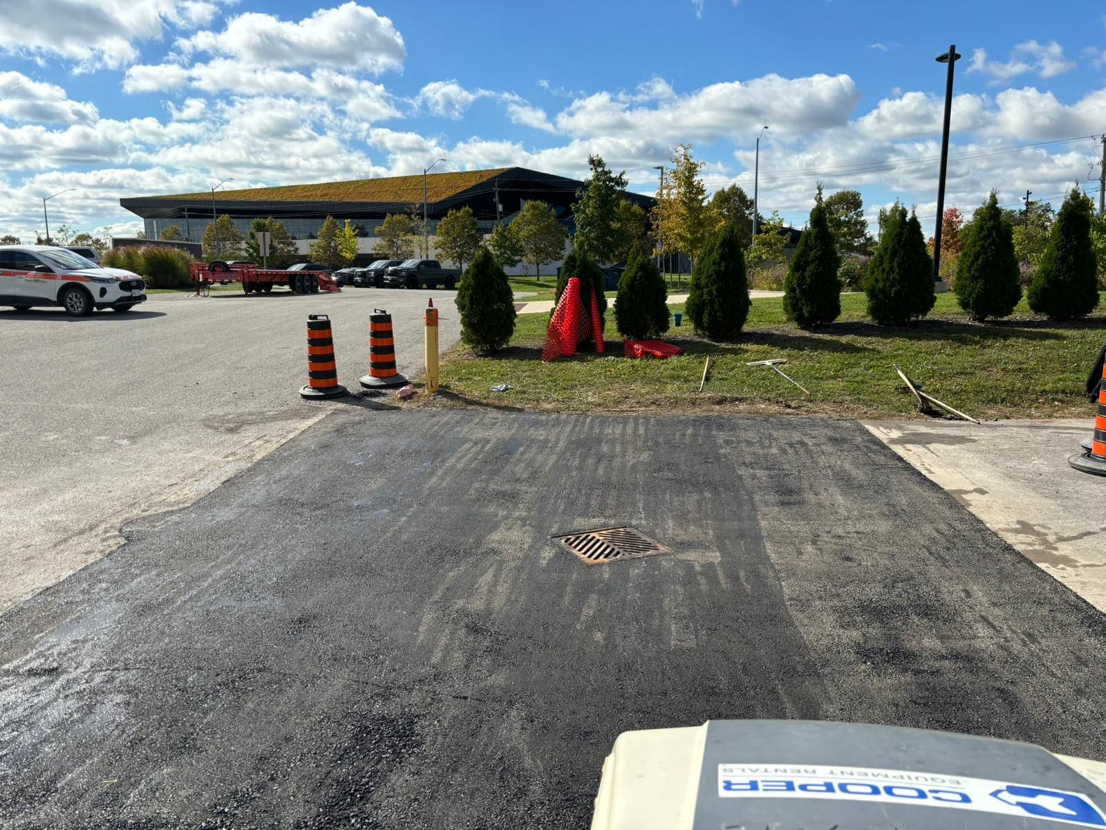 Freshly paved asphalt patch in a parking lot, near a building and traffic cones.