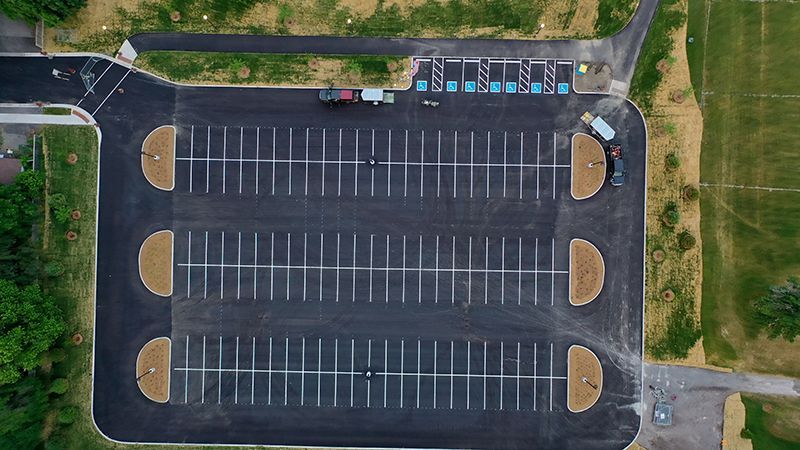 Aerial view of a mostly empty asphalt parking lot with multiple parking spaces and landscaped islands.