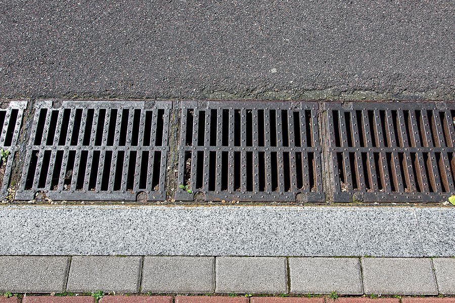 Grating drain on a street's edge, alongside brick and asphalt, collecting rainwater.