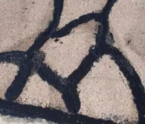 Dark, textured lines forming a geometric pattern on a light-colored, grainy surface.