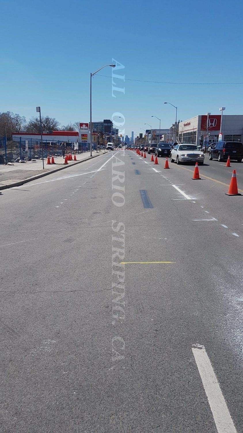 Road with traffic cones, cars, and gas station, under a bright blue sky.