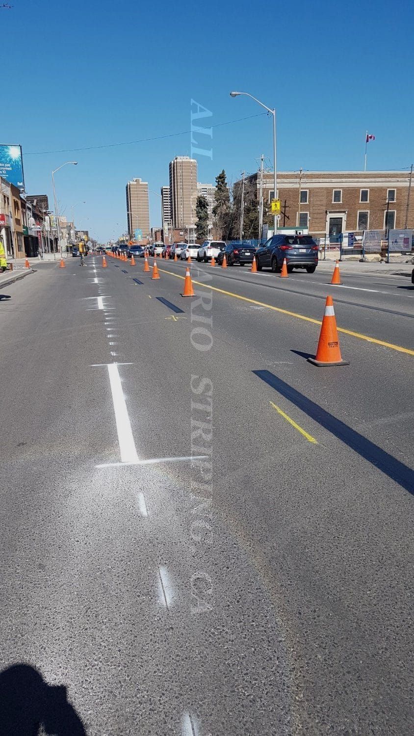 Street with orange traffic cones and marked lanes under a blue sky, likely road construction.