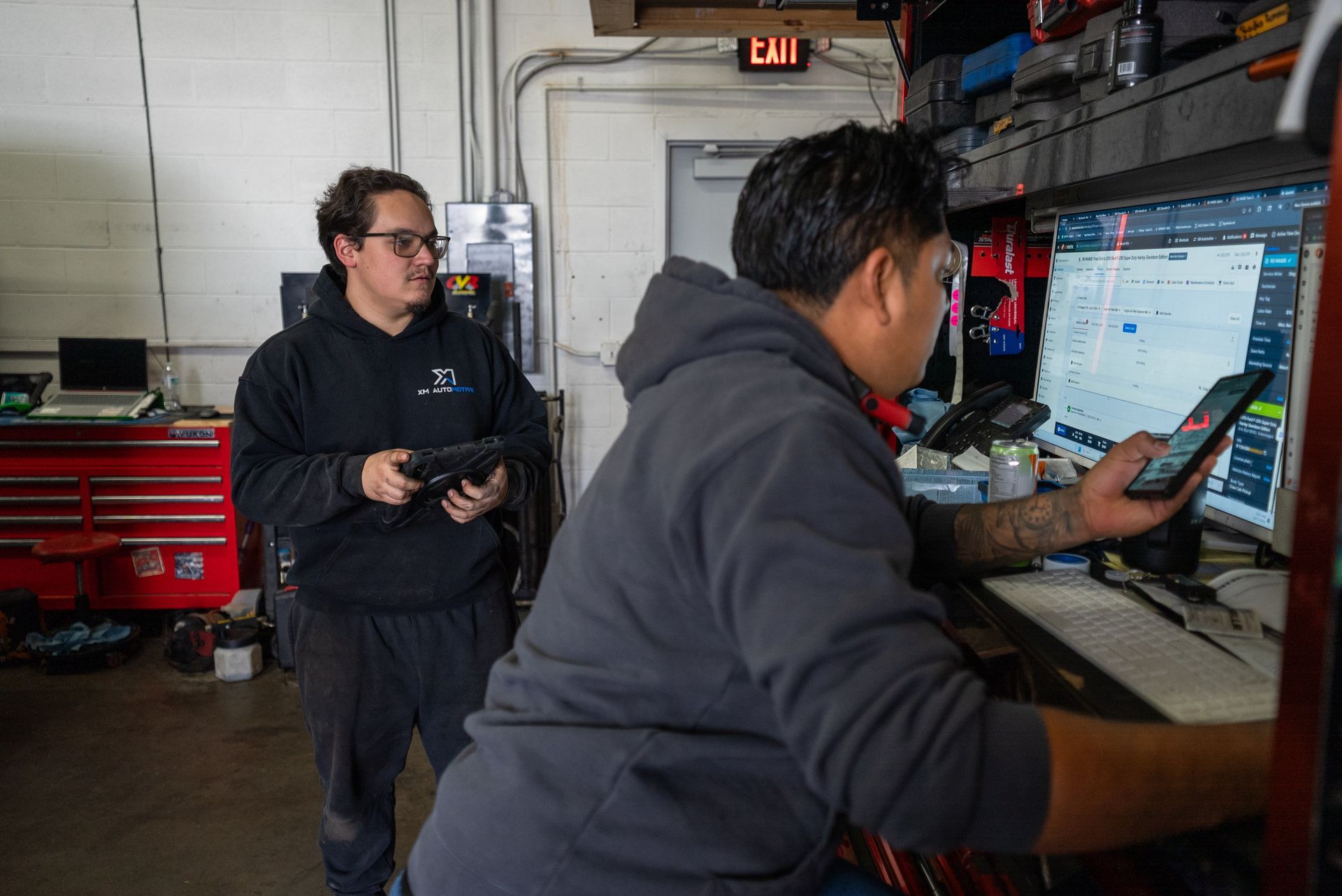 Two mechanics in a garage, one using a tablet, the other a phone and computer | Lenexa, KS