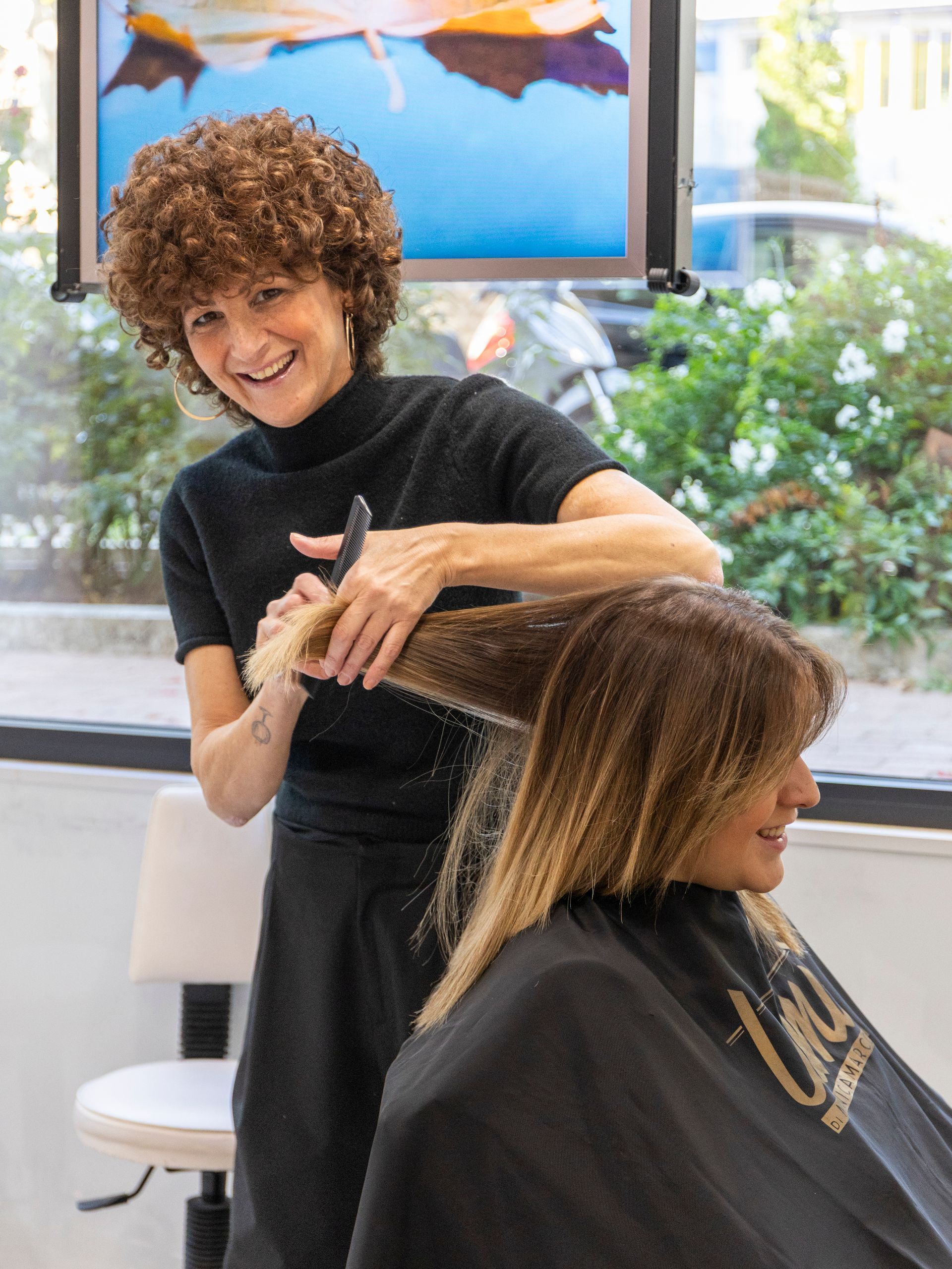 Una donna con i capelli ricci taglia i capelli ricci e viola di un'altra donna in un salone di bellezza.