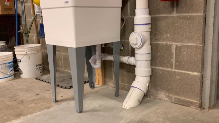 A white sink is sitting next to a pipe in a basement.