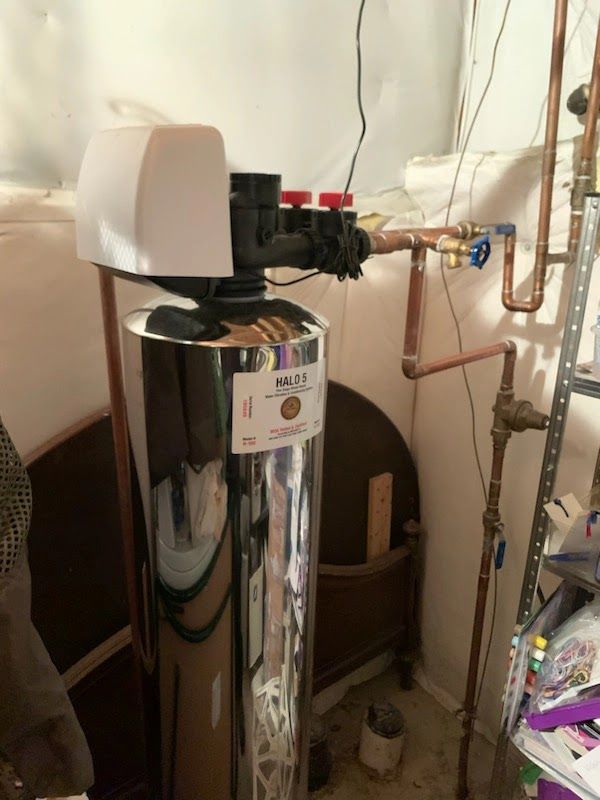 A water filter is sitting in a room next to copper pipes.