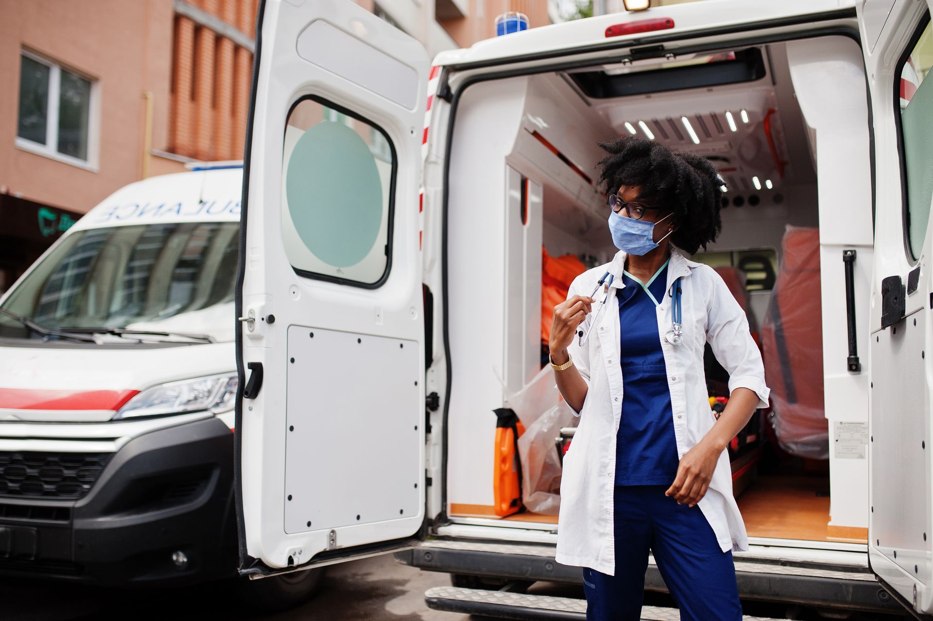 A doctor wearing a mask is standing in front of an ambulance.