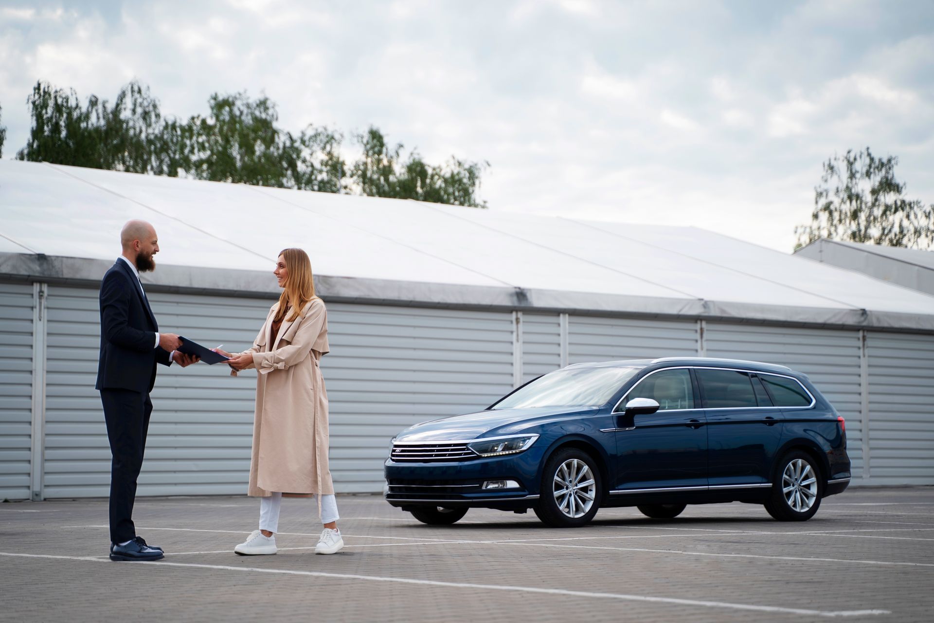 A man is shaking hands with a woman in front of a blue car.