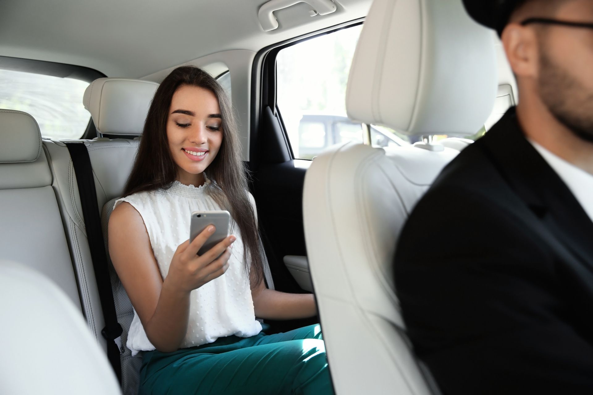 A woman is sitting in the back seat of a car looking at her cell phone.