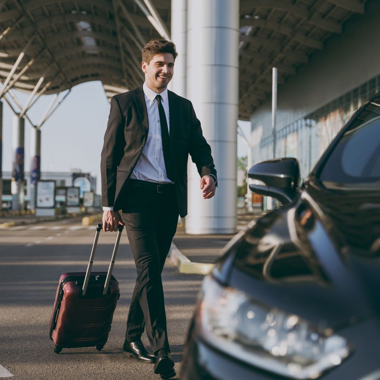 A man in a suit is pulling a suitcase next to a car