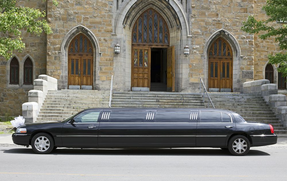 A black limousine is parked in front of a church.