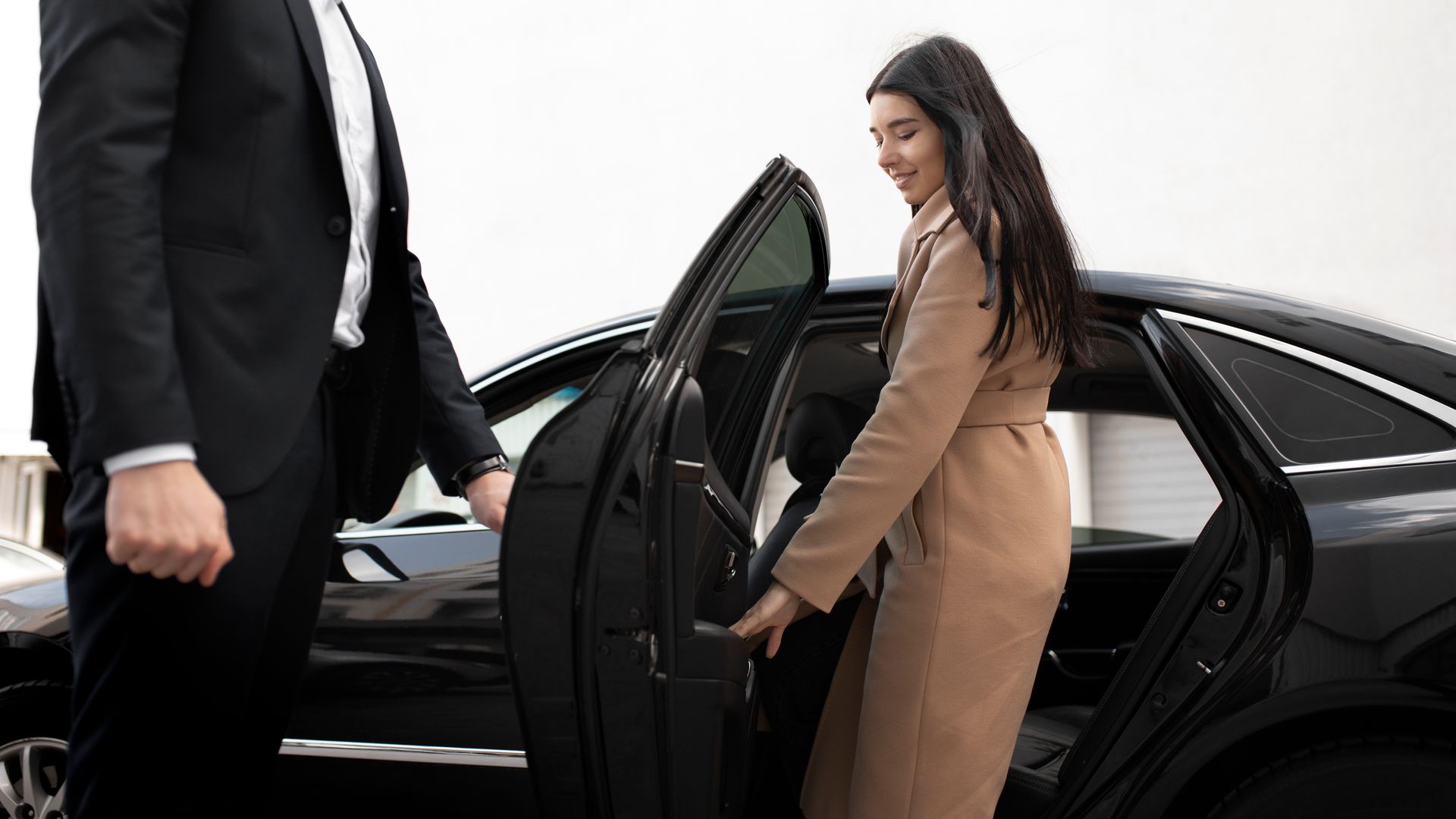 A woman is getting out of a car next to a man in a suit.