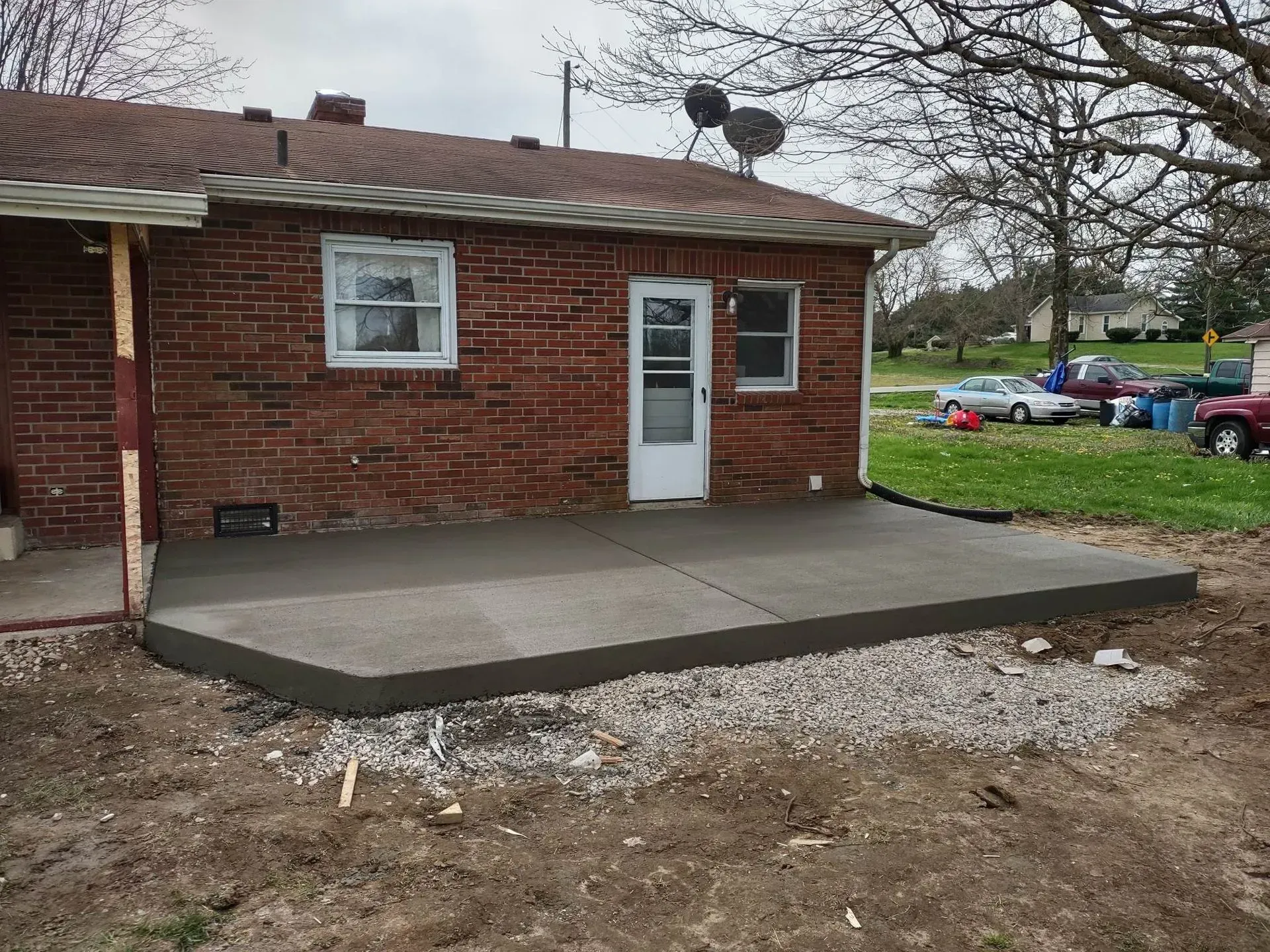 Brick house with a small concrete patio and white door beside a grassy yard.