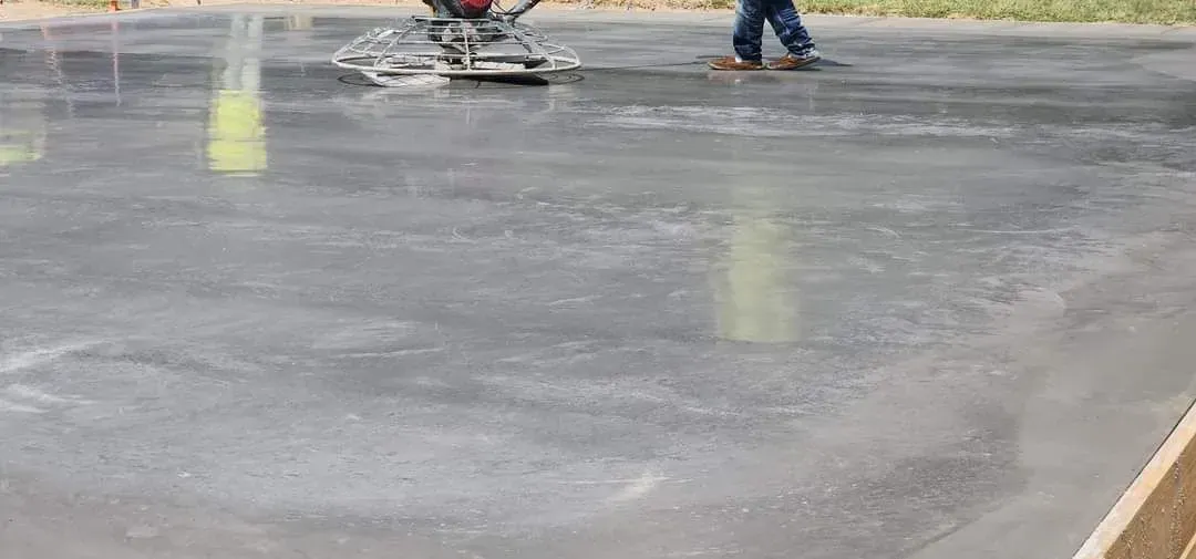 Workers smoothing wet gray concrete on a floor slab with yellow guide lines