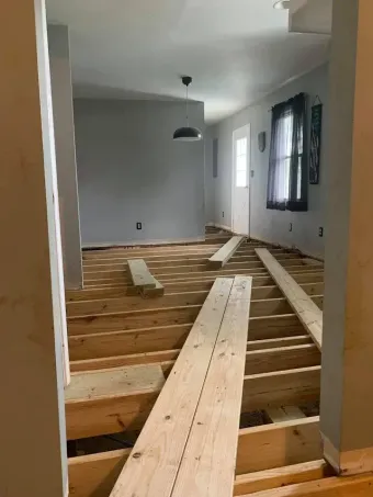 Partially renovated room with exposed floor joists and stacked wooden planks along the right wall