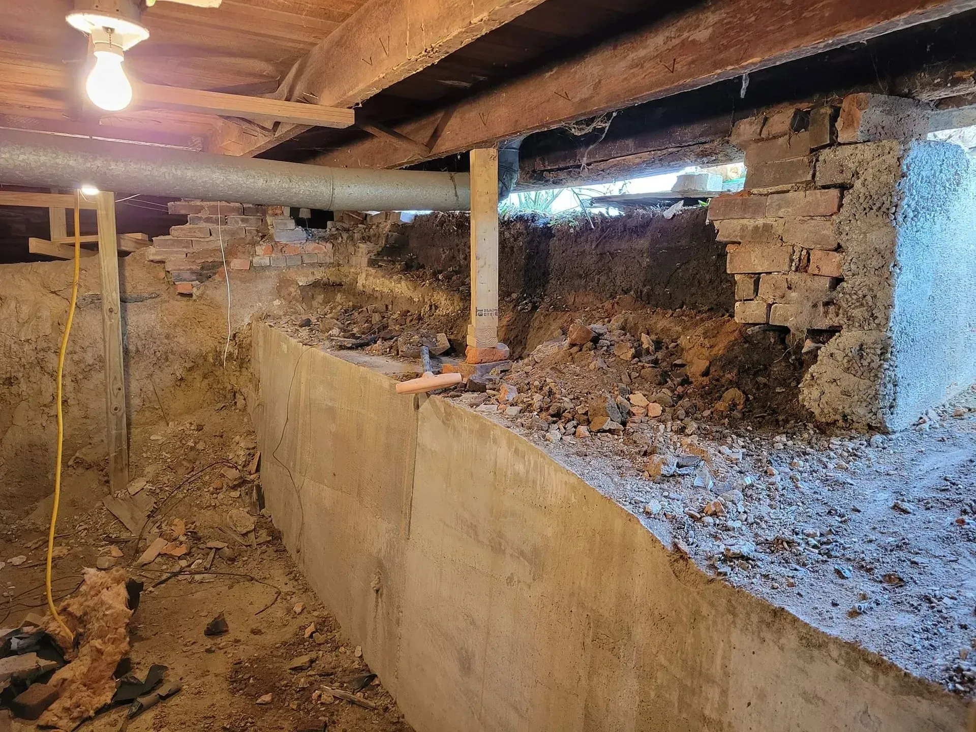 Crawlspace with exposed brick, concrete foundation wall, beams, and dirt floor under a house