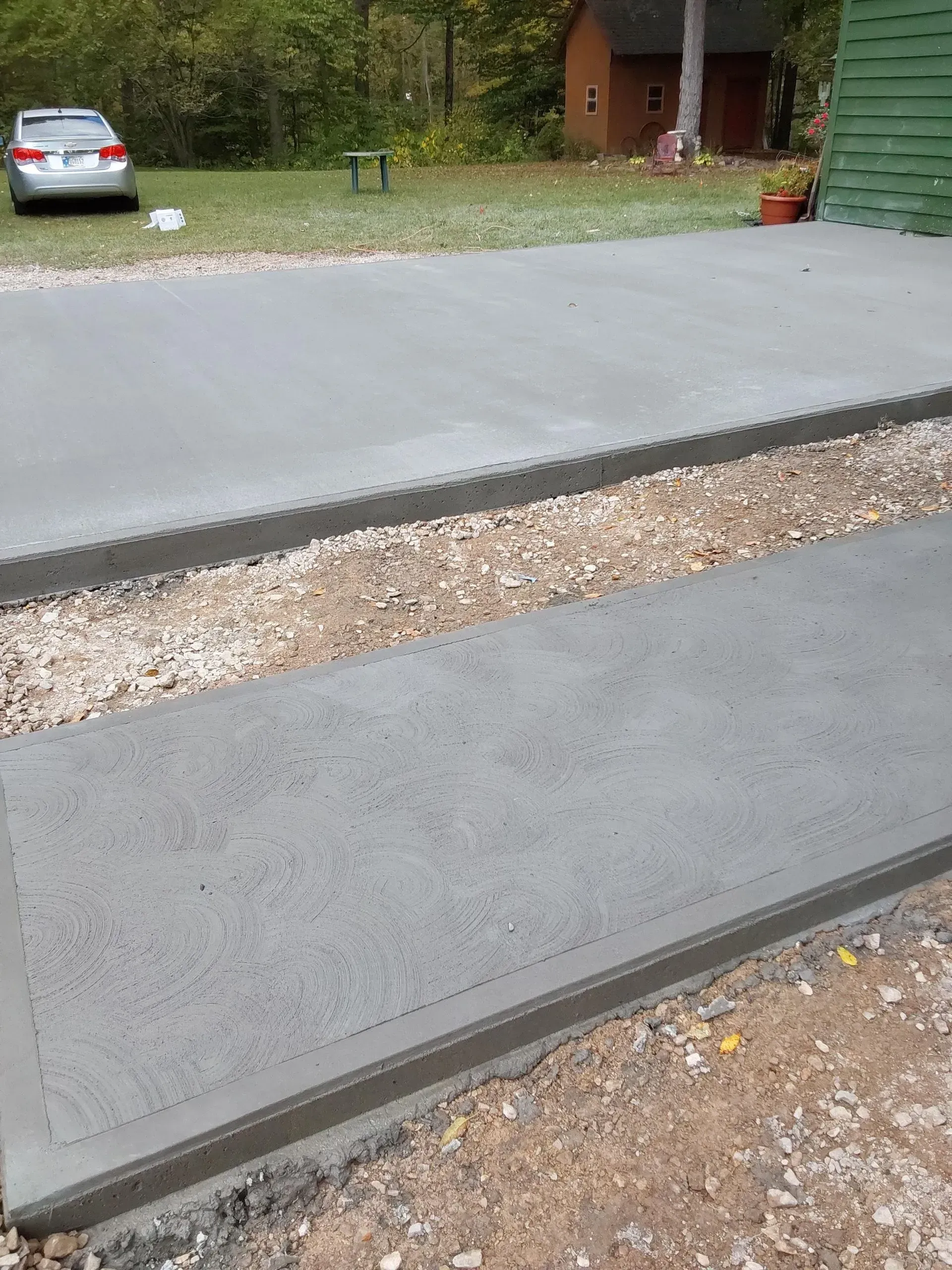 Concrete driveway with two raised curb-like strips and a parked silver car in the background