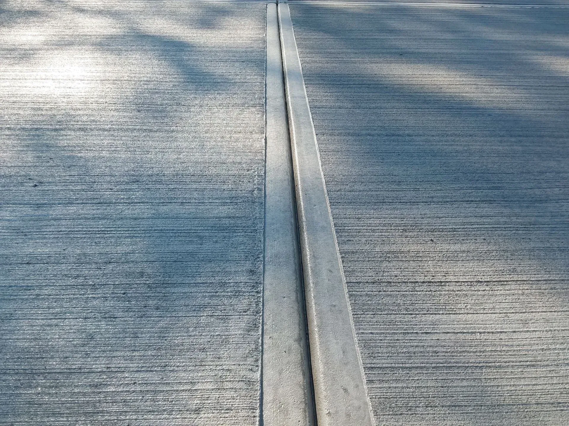 Close-up of a concrete road with a narrow metal joint running down the center