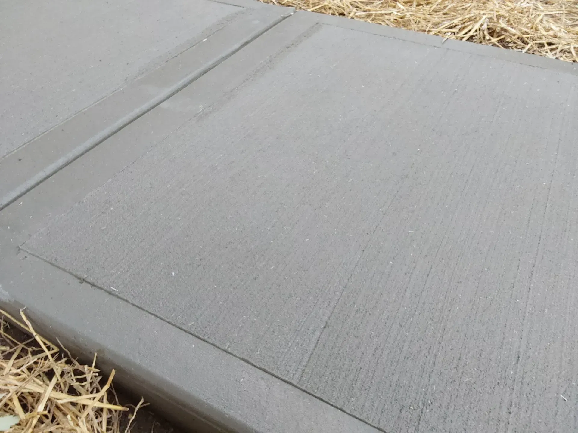 Gray concrete sidewalk corner beside straw-covered ground during construction work