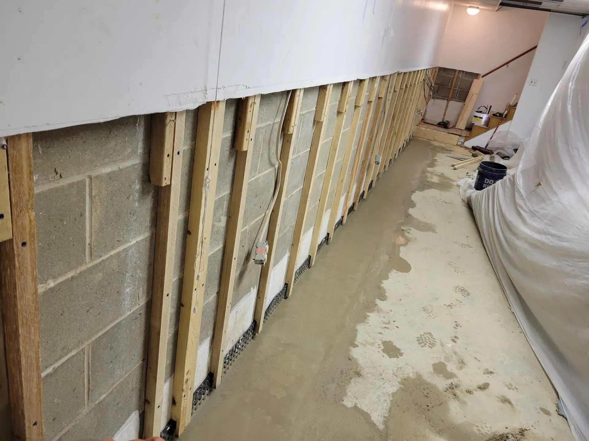 Partially stripped basement wall with exposed studs and cinder blocks along a concrete floor under renovation
