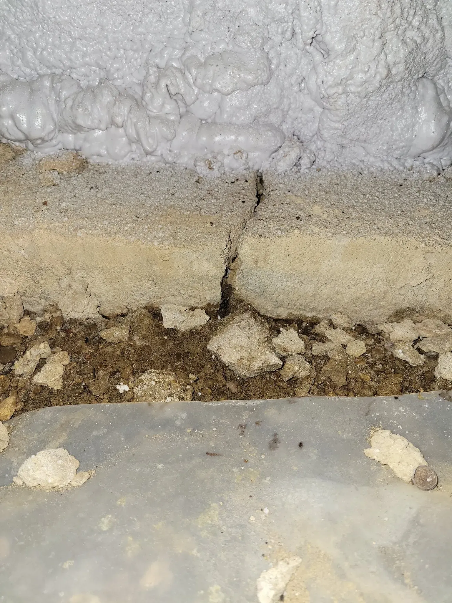 Cracked wall with white insulation above and a rough brown gap at the base