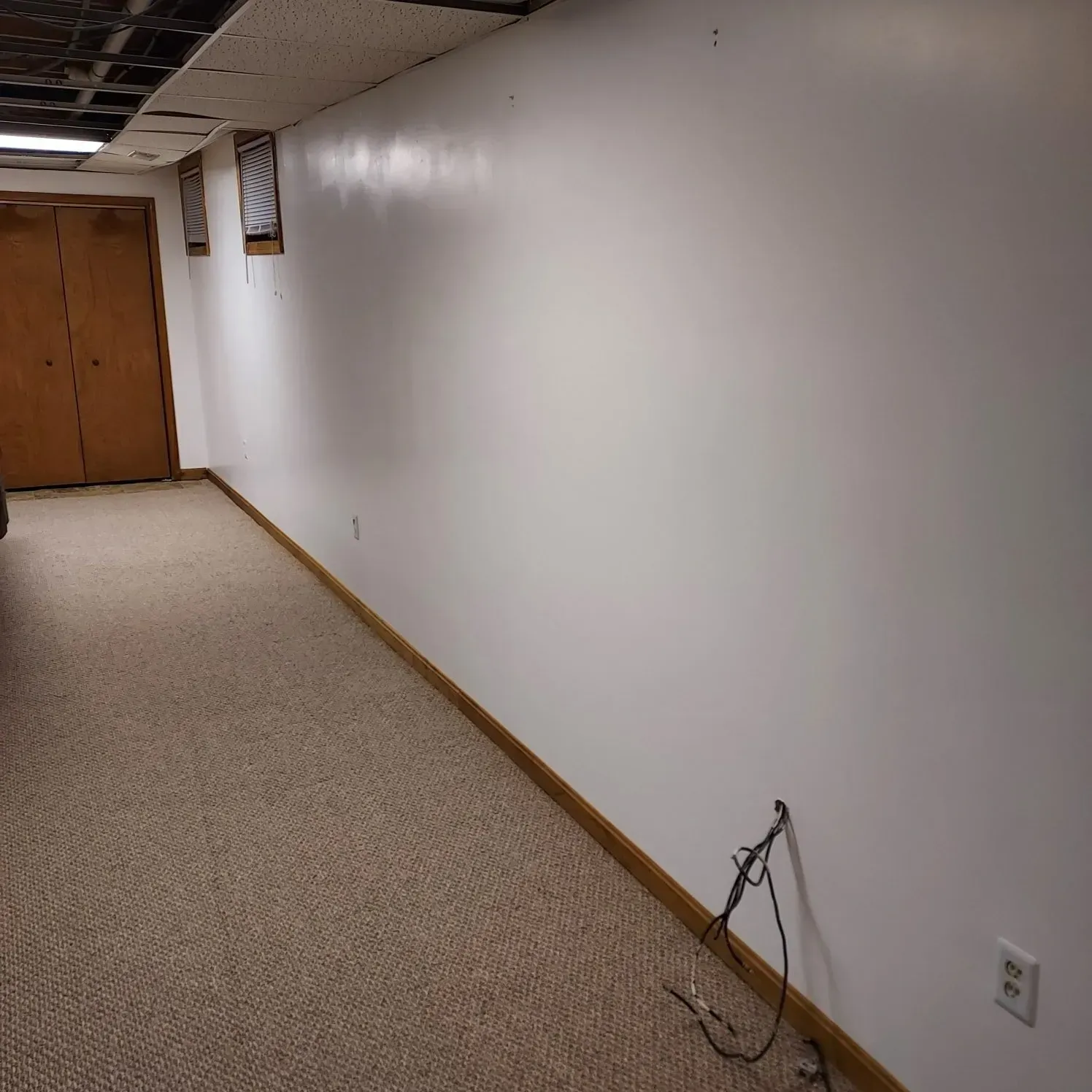 Empty hallway with white wall, carpeted floor, and a dangling cable near the baseboard.