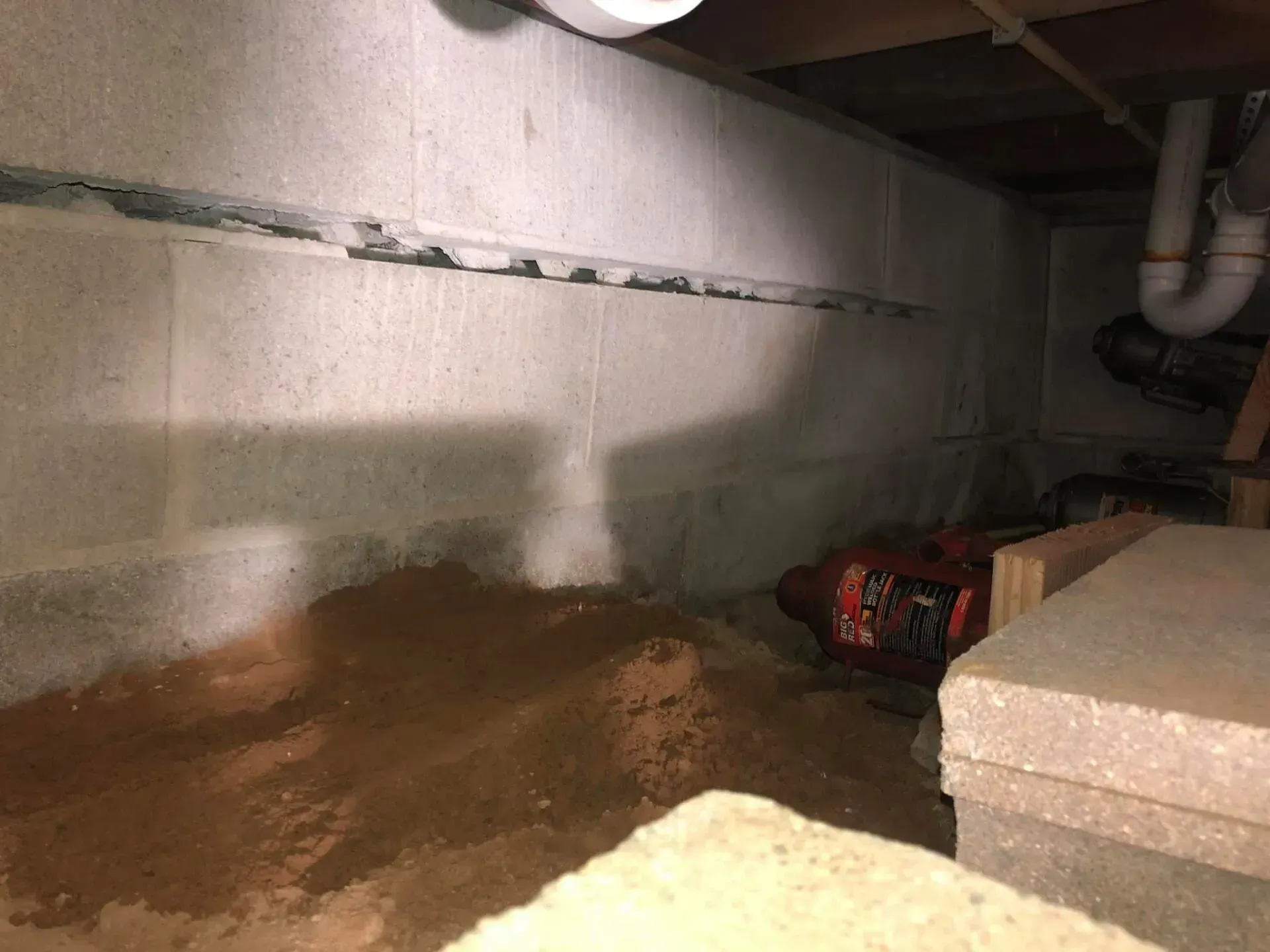 Basement crawlspace with a damp concrete wall, puddled floor, and stacked foam boards on the right