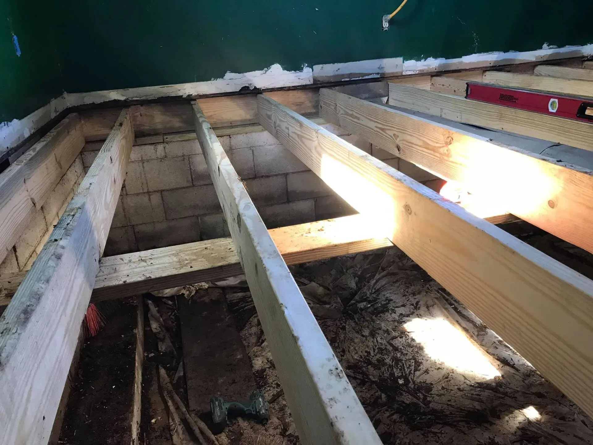 Exposed floor joists and beams under construction with sunlight streaming through gaps.