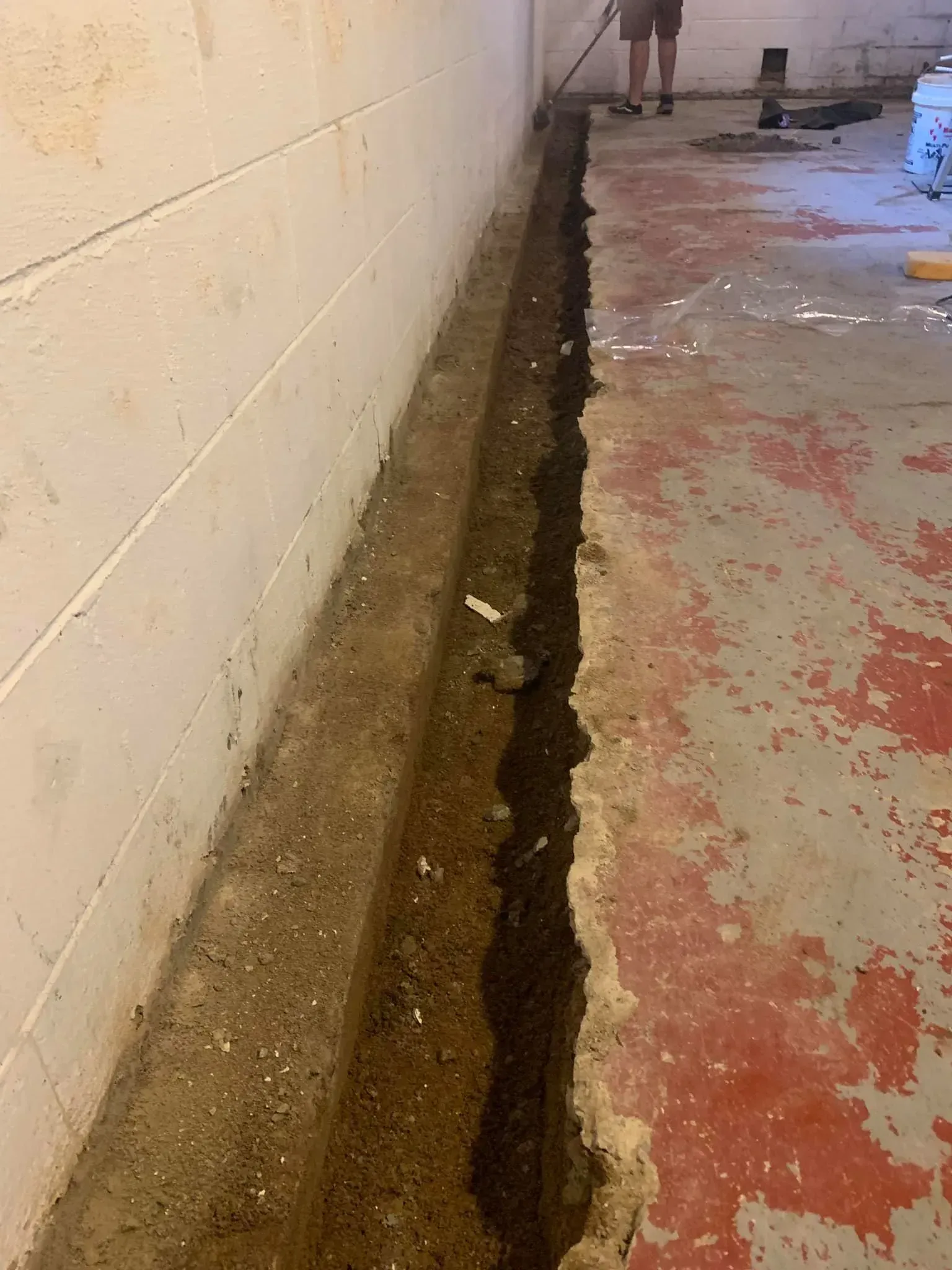 Damaged concrete floor with a long trench or crack along a wall in an indoor corridor.
