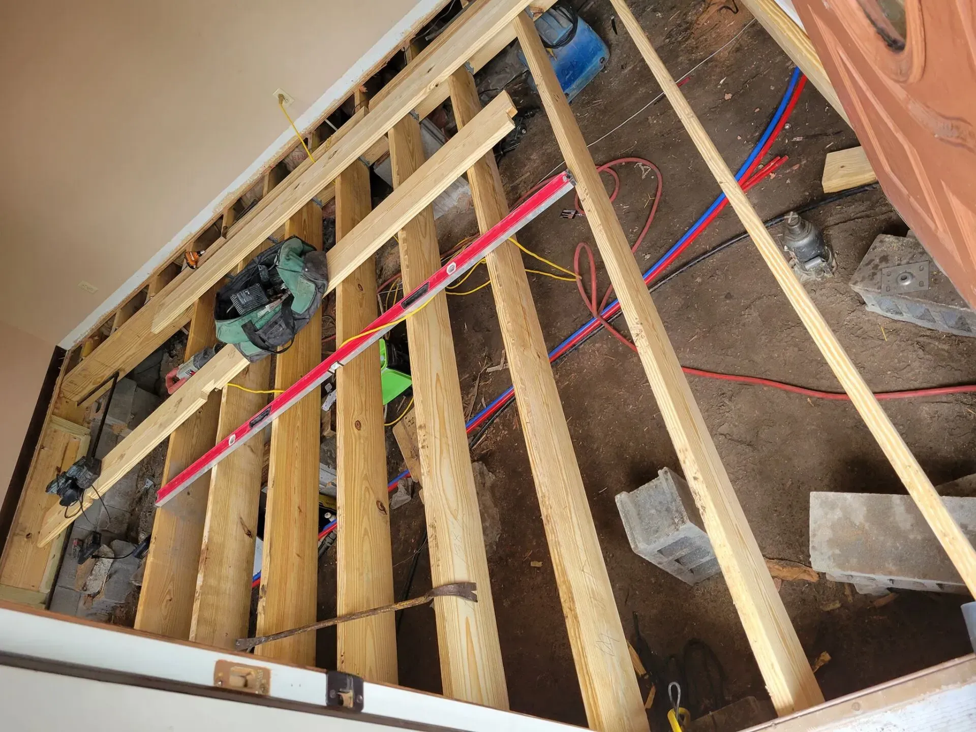 Open floor joists in a construction site with exposed wiring, insulation, and a power tool.