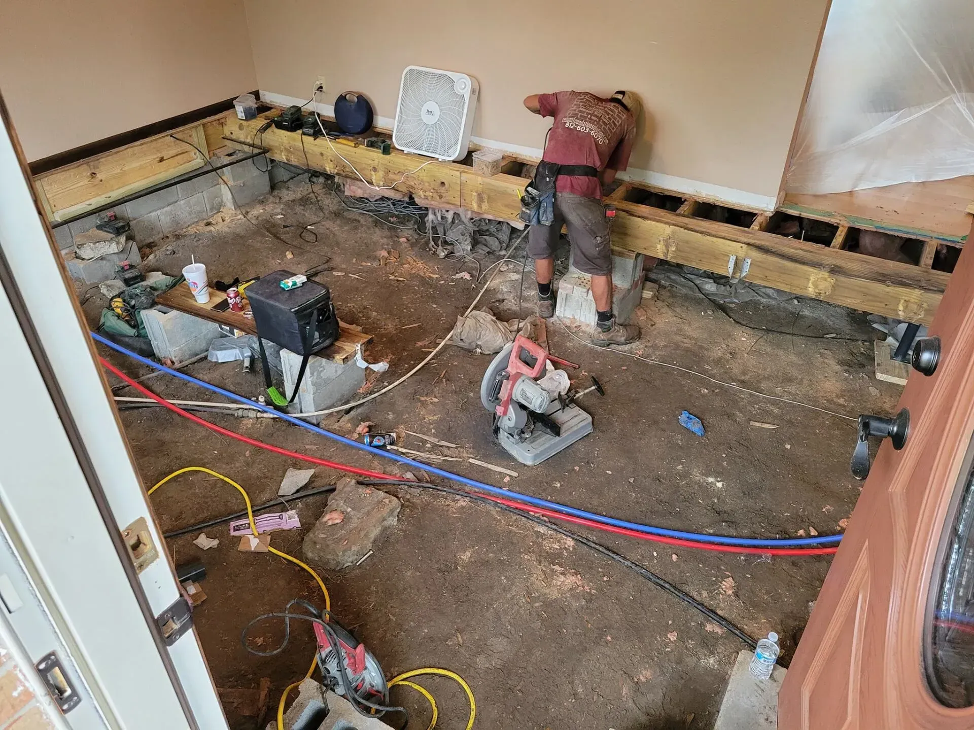 Renovation scene with workers and tools in a stripped room with exposed floor and wiring