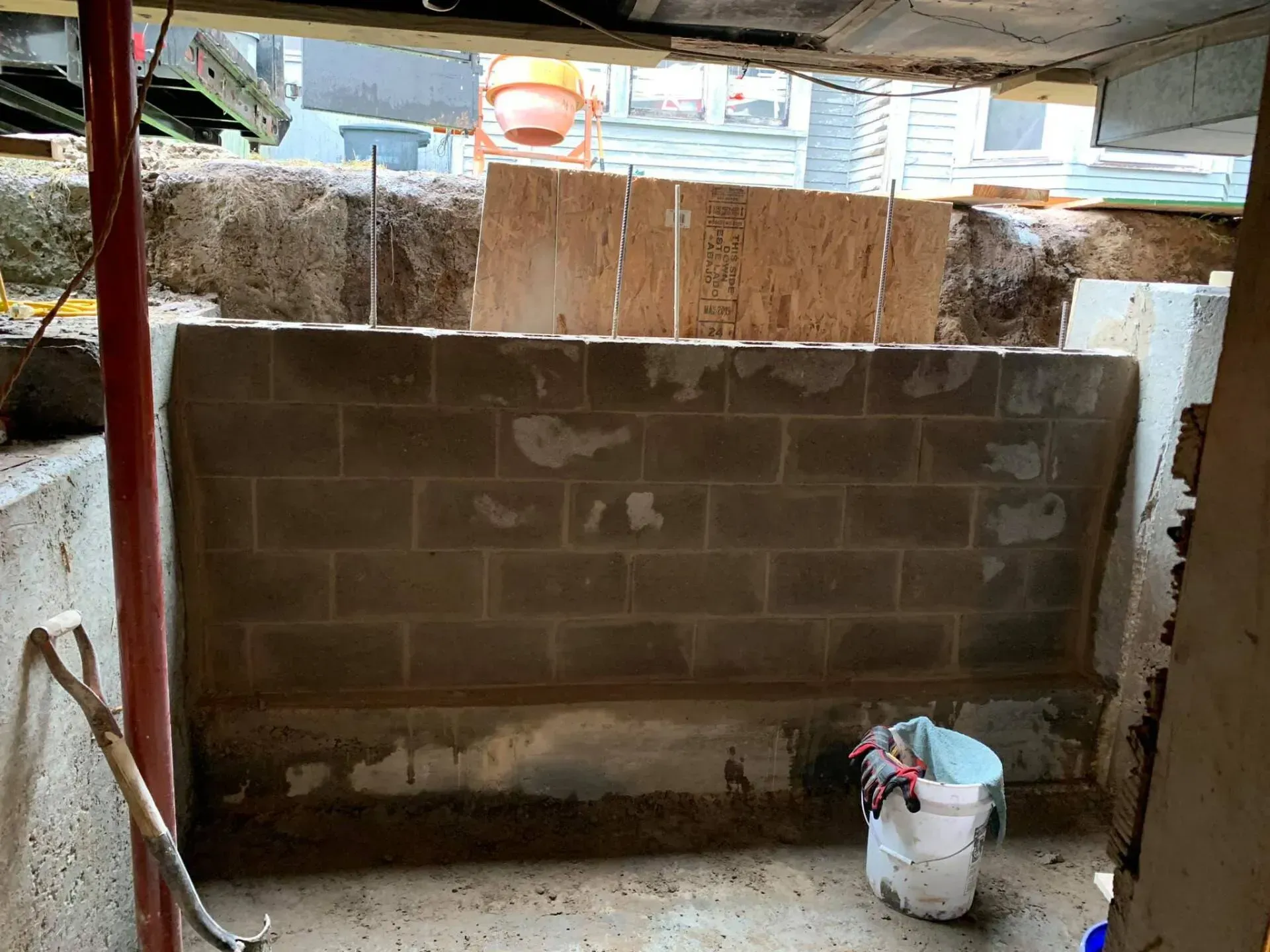 Unfinished cinder block wall in a construction area, with a white bucket on the floor and wooden boards above.