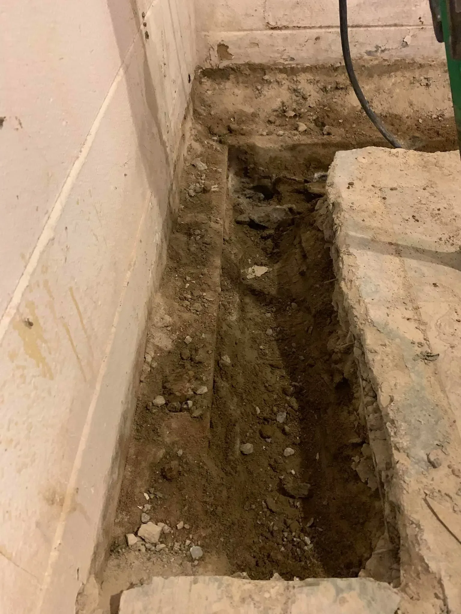 Narrow dirt trench dug beside a wall and concrete steps indoors