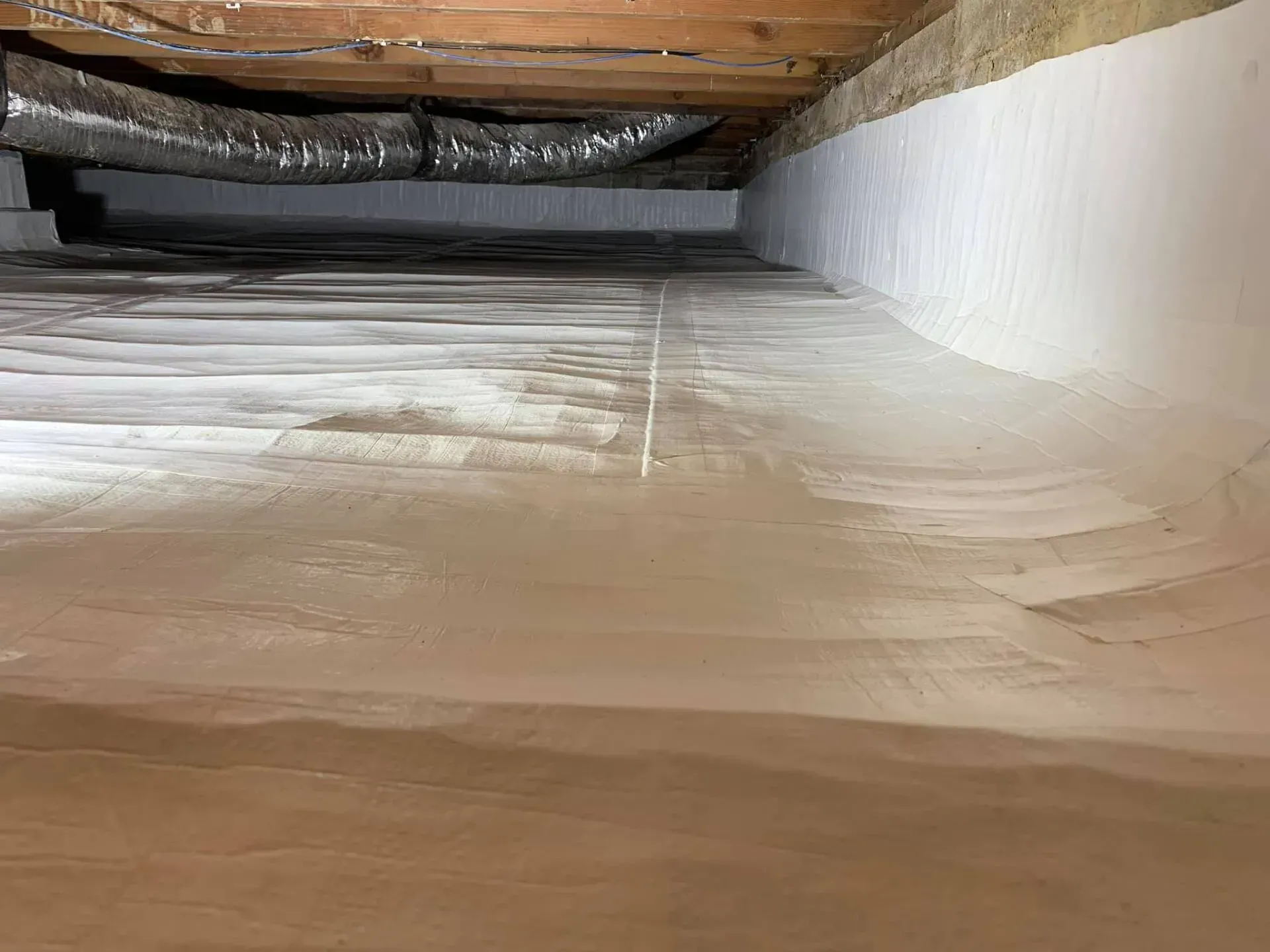 Insulated attic crawlspace with wooden beams and white spray foam along the walls and floor.