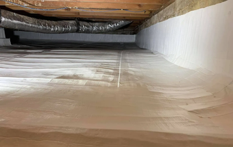 Attic crawl space with white spray foam insulation on the walls and ceiling joists above.