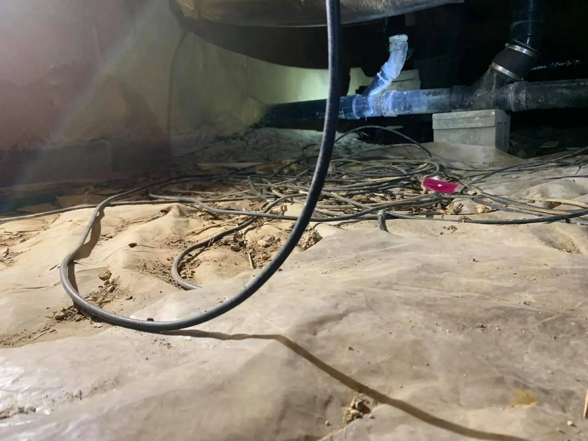 Dusty floor with a coiled black cable and scattered debris under a piece of furniture