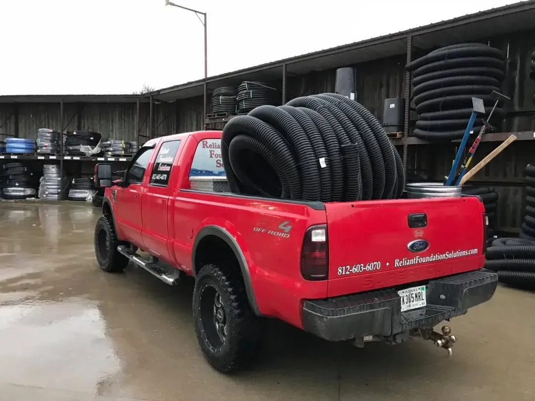 Red pickup truck loaded with large black coiled hoses in a wet industrial yard