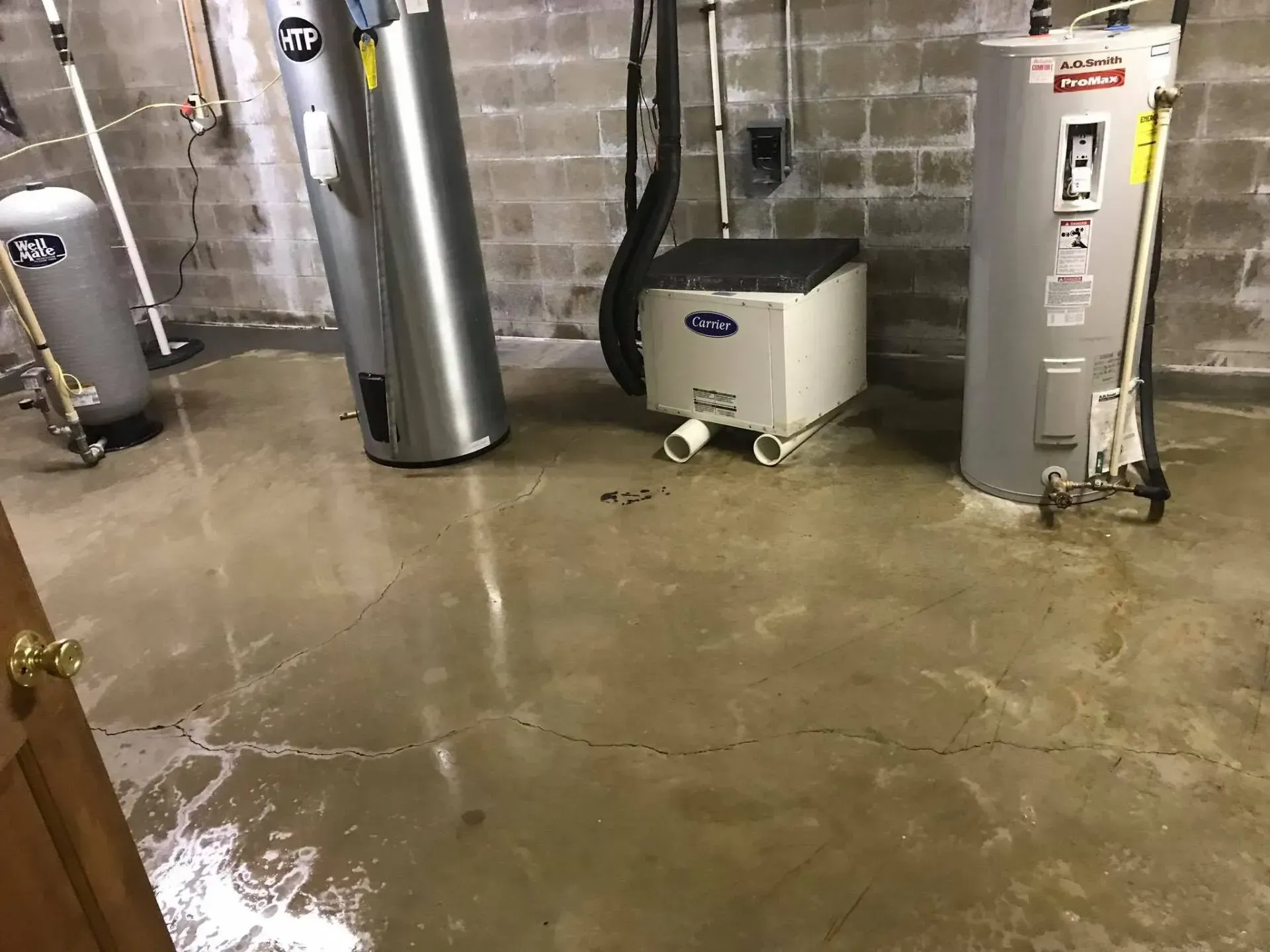 Basement utility room with water on the floor, a water heater, boiler, and furnace against concrete walls.