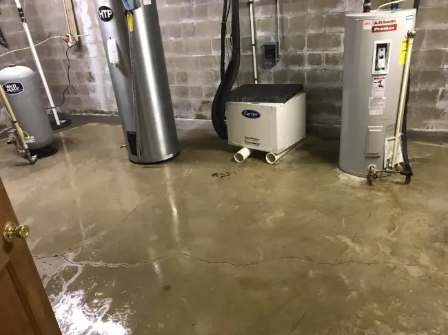 Flooded basement with water on the concrete floor, near a water heater and HVAC equipment.